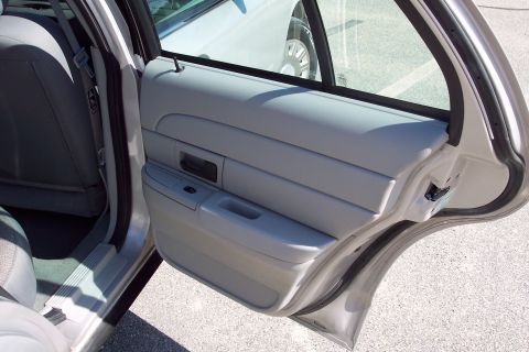 2001 Ford Crown Victoria - The interior door panel of a gray sedan is shown, featuring a black interior door handle and window controls. The open door reveals the car…