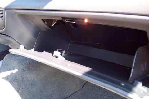 2001 Ford Crown Victoria - The open glove compartment of a car, showing the interior storage space and a small light illuminated inside. The glove box door is partial…