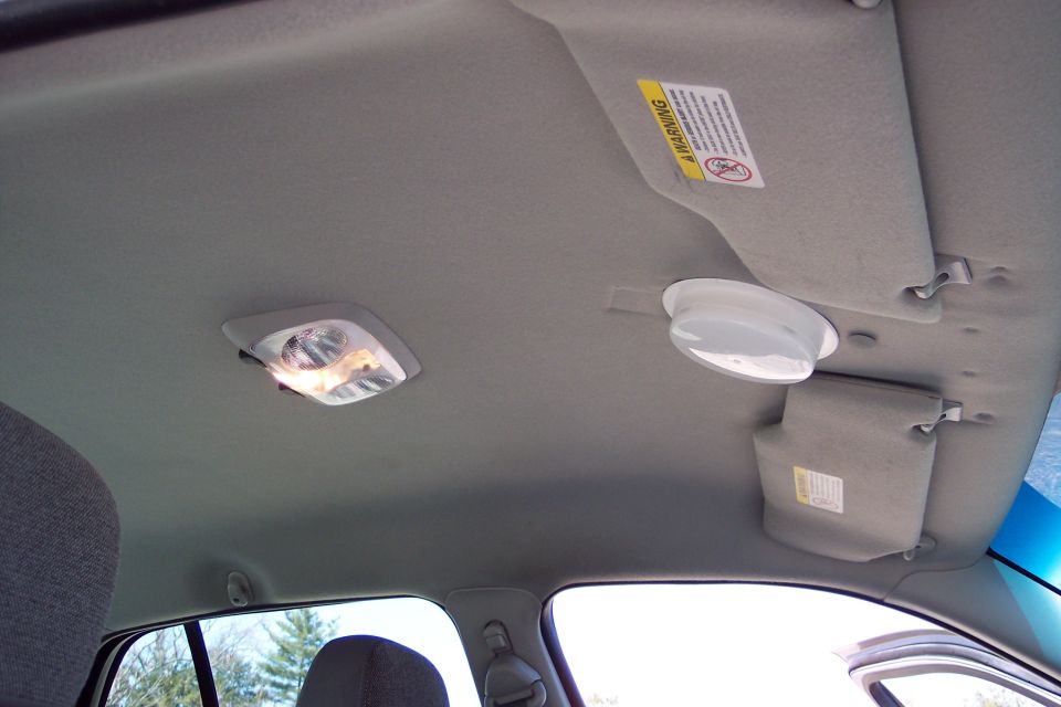 Interior of a car showing the headliner, dome lights, and a sun visor with a warning sticker.