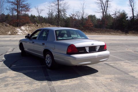 2001 Ford Crown Victoria - The rear passenger side of a silver 2001 Ford Crown Victoria is shown parked in an outdoor lot. The car is angled away from the camera, wit…