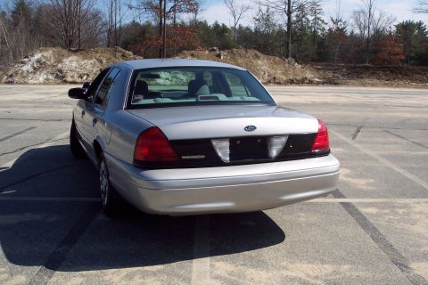 2001 Ford Crown Victoria - The rear driver's side of a silver 2001 Ford Crown Victoria Police Interceptor is shown parked in an outdoor lot. The car is angled away fr…