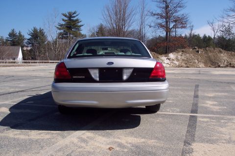 2001 Ford Crown Victoria - The rear view of a silver 2001 Ford Crown Victoria is shown parked in an asphalt lot. The car has a black panel between the taillights and…