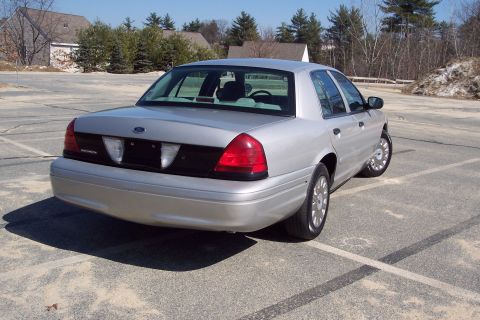 2001 Ford Crown Victoria - The rear passenger side of a silver Ford Crown Victoria is shown parked in an outdoor lot. The car is angled away from the camera, with the…