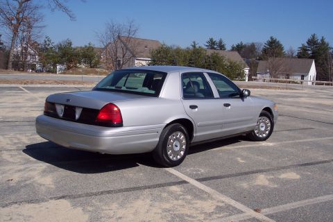 2001 Ford Crown Victoria - A silver 2001 Ford Crown Victoria sedan is parked in an outdoor asphalt lot. The rear passenger side of the vehicle is visible, with a clea…