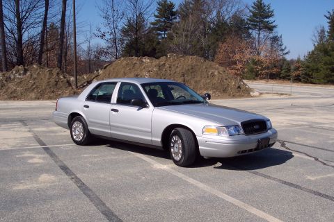 2001 Ford Crown Victoria - A silver 2001 Ford Crown Victoria sedan is parked in an outdoor paved lot with tire marks visible on the ground. The vehicle is viewed from…