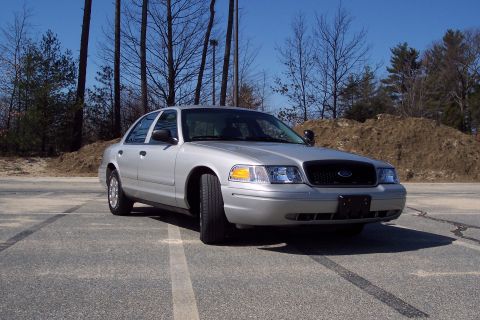 2001 Ford Crown Victoria - A silver 2001 Ford Crown Victoria sedan is parked on an asphalt lot with tire marks. The car is viewed from a 3/4 front angle, showcasing i…