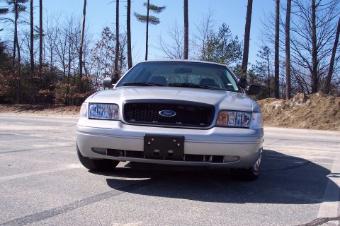 2001 Ford Crown Victoria - Front view of a silver 2001 Ford Crown Victoria parked on asphalt with tire marks. The car has a black grille with a Ford emblem and a lice…