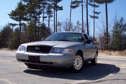 2001 Ford Crown Victoria - A silver 2001 Ford Crown Victoria sedan is parked on an asphalt surface with trees in the background.