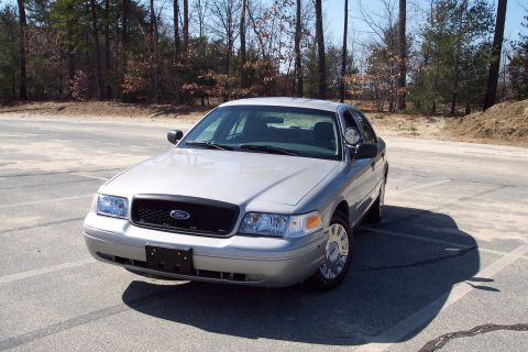 2001 Ford Crown Victoria - A silver 2001 Ford Crown Victoria sedan is parked on a paved surface with painted lines, facing slightly left. The vehicle has a black gril…