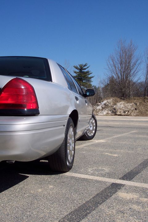 2001 Ford Crown Victoria - The rear passenger side of a silver 2001 Ford Crown Victoria is shown parked in a lot on a sunny day. The car is viewed from a low angle, h…