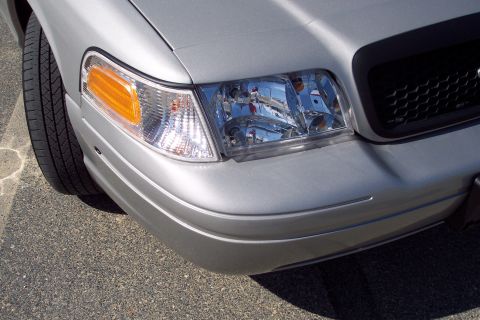 2001 Ford Crown Victoria - A close-up, low-angle shot of the front passenger side corner of a silver Ford Crown Victoria. The image shows the headlight assembly, turn…