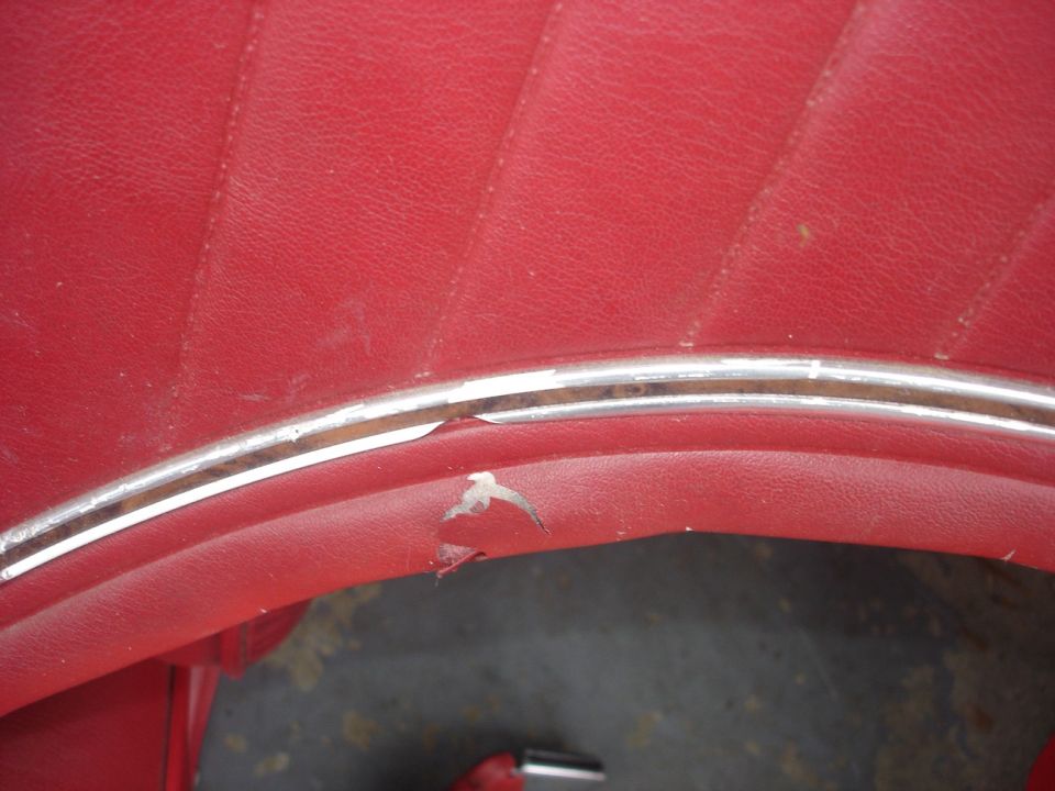 Close-up of red vinyl upholstery with chrome trim and a tear.