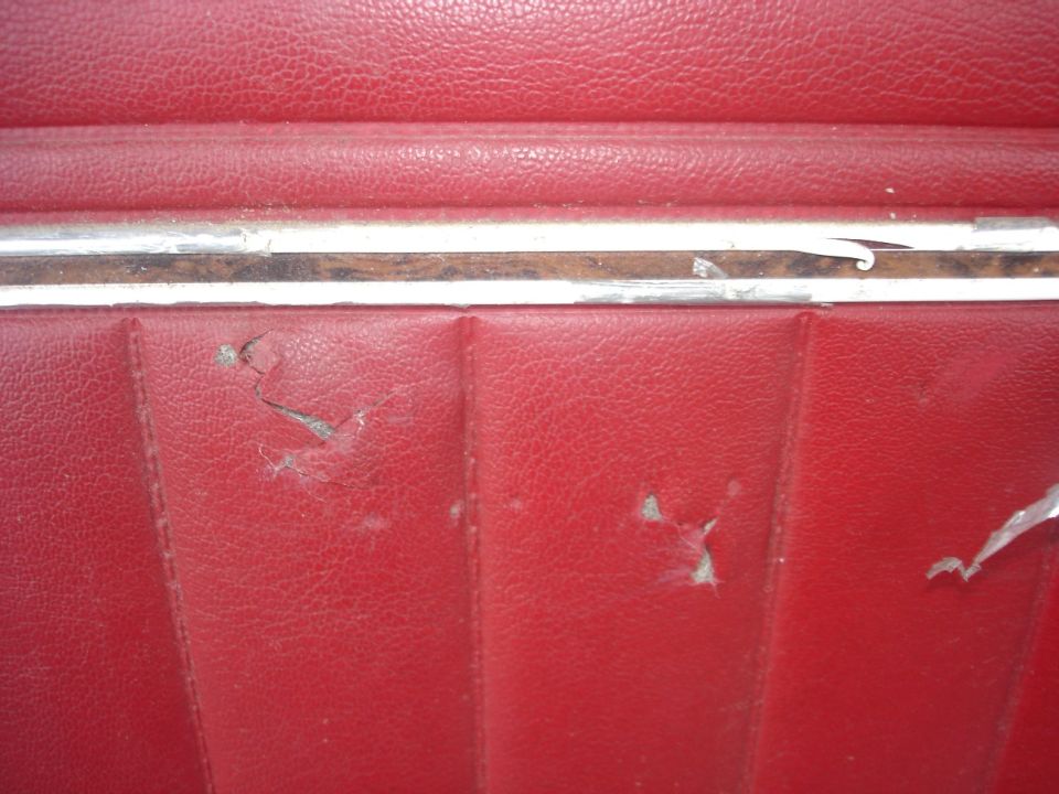 Close-up of damaged red vinyl interior panel with chrome trim.