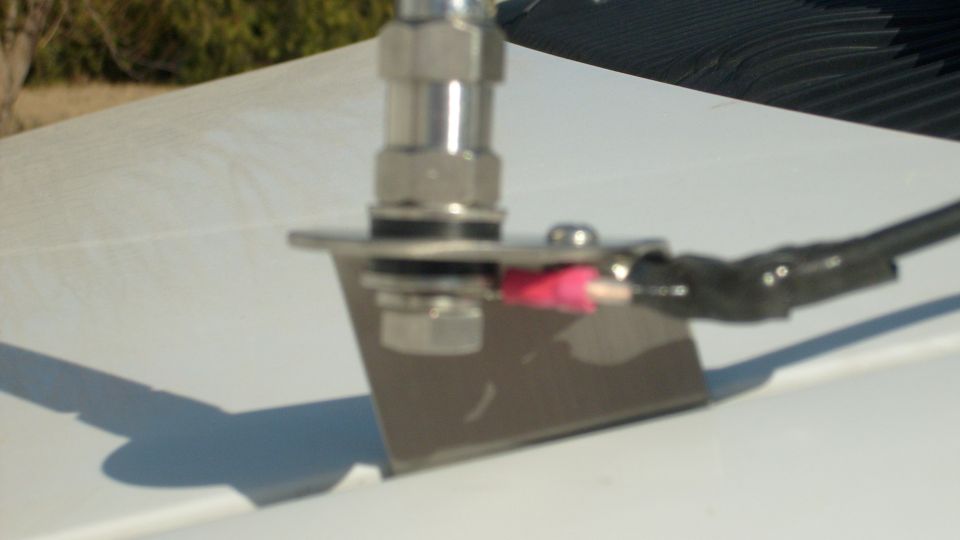 Close-up of a metal antenna mount attached to a white surface, with red wire connectors and black electrical tape