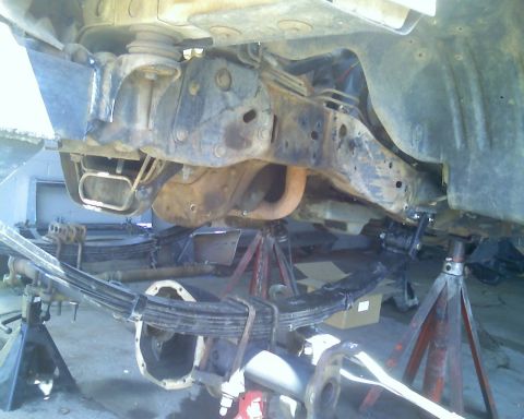 1996 Ford Bronco - The vehicle's undercarriage is visible, supported by jack stands, with leaf springs and differential exposed.