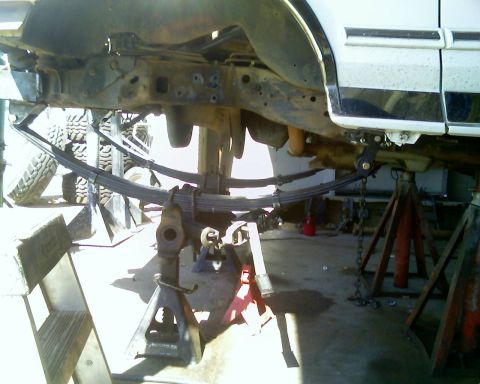 1996 Ford Bronco - The underside of a white vehicle is elevated on jack stands, revealing its suspension system with prominent leaf springs.