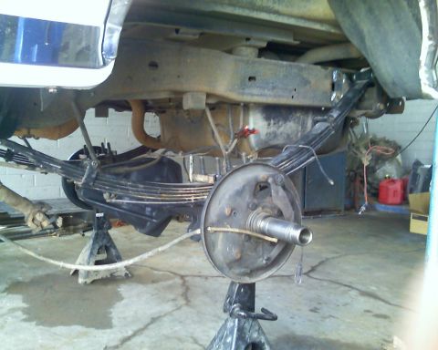 1996 Ford Bronco - The rear suspension and axle assembly of a vehicle are visible while it is supported by jack stands in a garage.