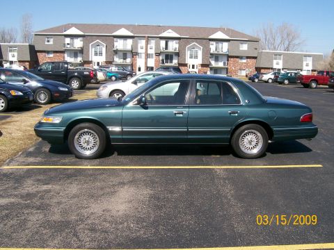 1995 Mercury Grand Marquis - A 1995 Mercury Grand Marquis is parked in a lot with other vehicles and an apartment building in the background.