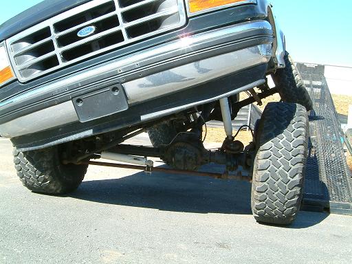 Lifted dark Ford Bronco flexing suspension with front wheel on a ramp, showing chrome grille and large mud tires