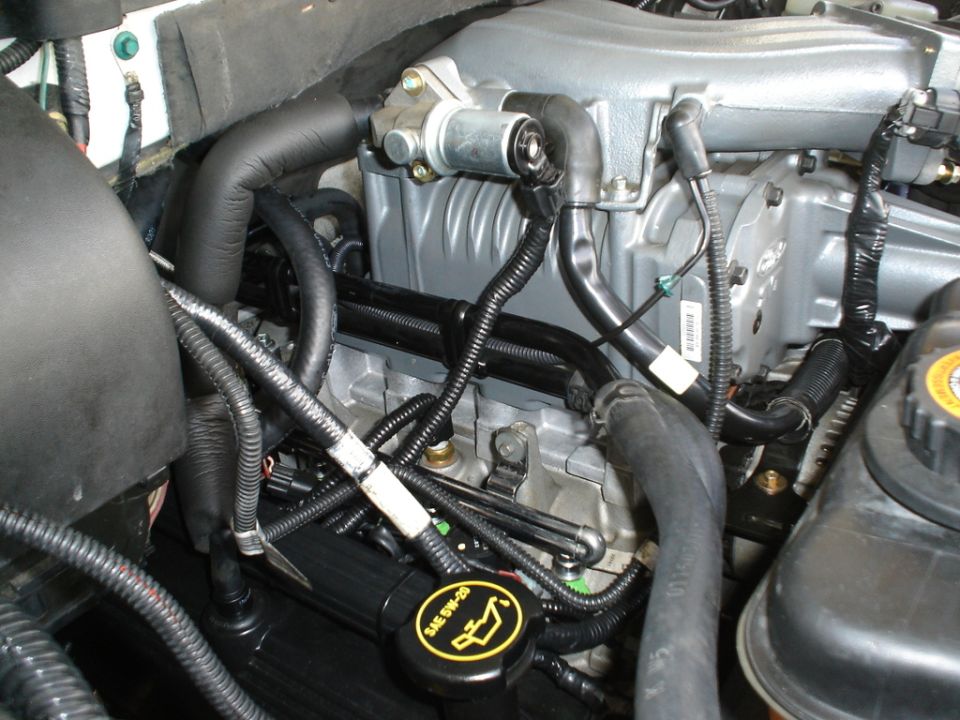 Close-up of a supercharged engine bay, showing hoses, wiring, and a black oil cap with yellow markings