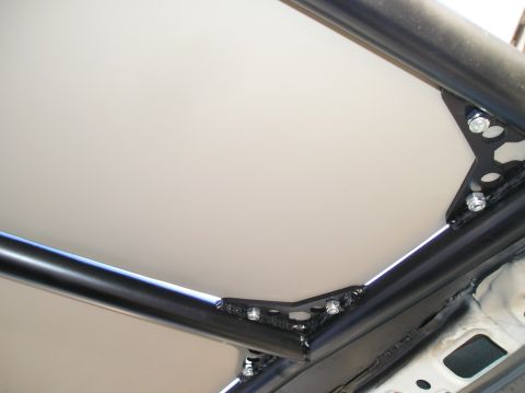 1986 Toyota Hilux - The interior of a vehicle shows a custom roll cage with bolted metal brackets and a light-colored panel.