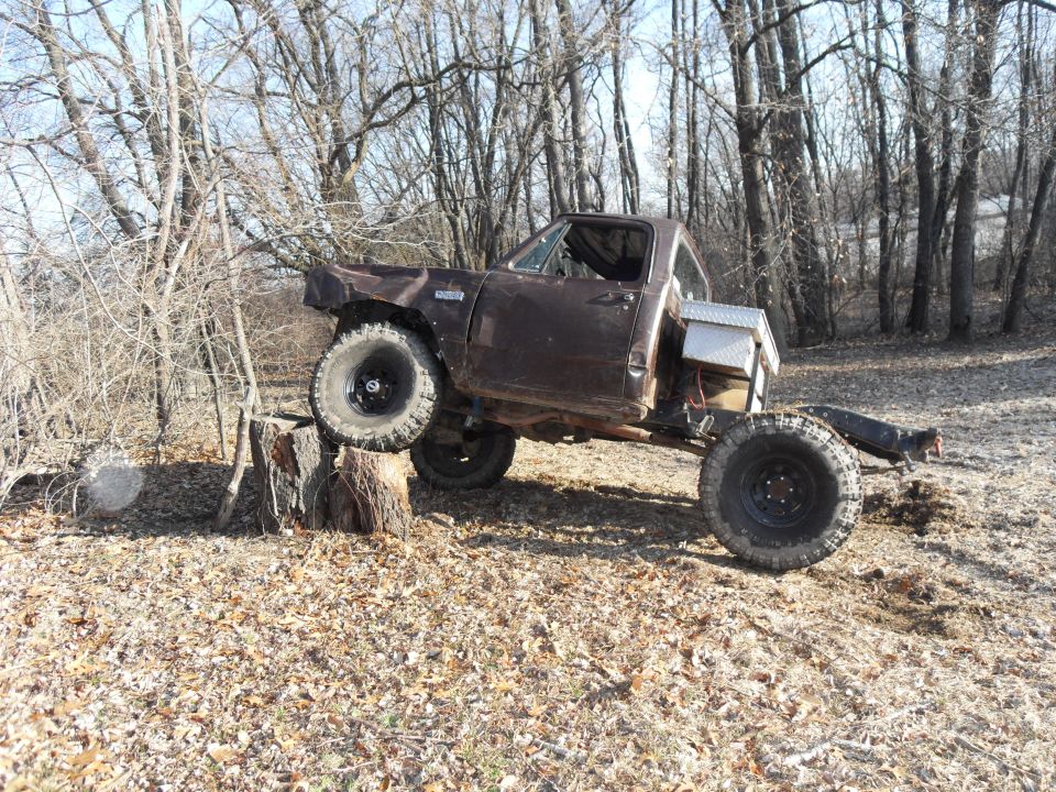 Brown pickup truck with large tires on a stump, off-road modifications visible