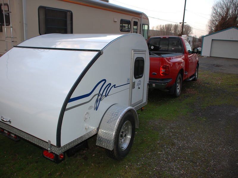 Red pickup truck towing a white teardrop trailer. The truck is a 1997 Ford F-150