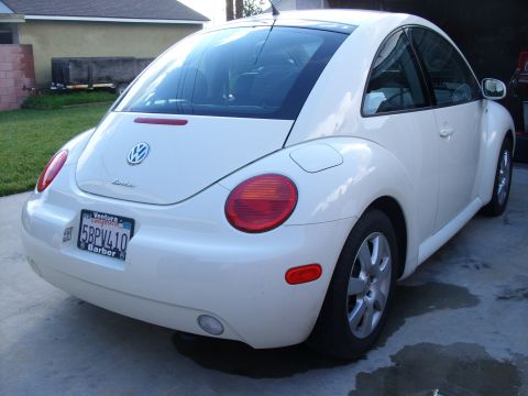 2003 Volkswagen Beetle - The rear of a white Volkswagen Beetle is shown parked in a driveway, with a house and lawn in the background.
