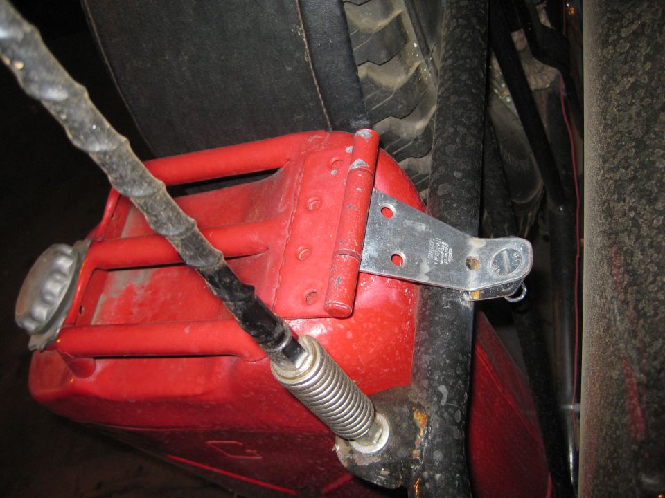 Red jerrycan with metal strap and spring-loaded mechanism attached to vehicle frame