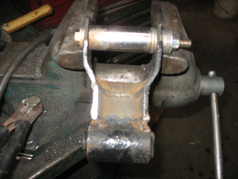 Suspension part held in a vise, showing a metal bracket and bolt
