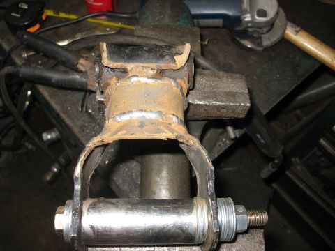 1995 Ford C-350 (Centurion Conversions) - A heavily rusted suspension part, likely from a vehicle, is held in a vise with new hardware attached.