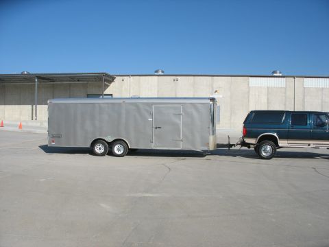 1995 Ford C-350 (Centurion Conversions) - A teal Ford Bronco tows a dual-axle cargo trailer in front of a concrete building.