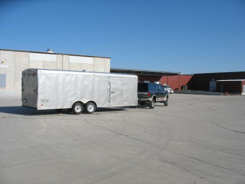 1995 Ford C-350 (Centurion Conversions) - A Ford F-350 pickup truck tows a large silver enclosed trailer in an industrial area under a clear blue sky.