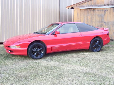 1996 Ford Probe - This red 1996 Ford Probe is captured in a 3q front view, parked on grass with a building in the background.