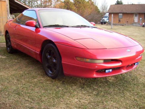 1996 Ford Probe - A red 1996 Ford Probe is parked outside on a grassy area near a building.