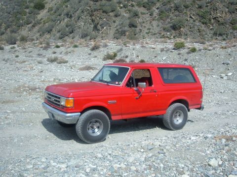 1988 Ford Bronco - This red 1988 Ford Bronco is parked on a rocky, unpaved road in a hilly, arid environment.