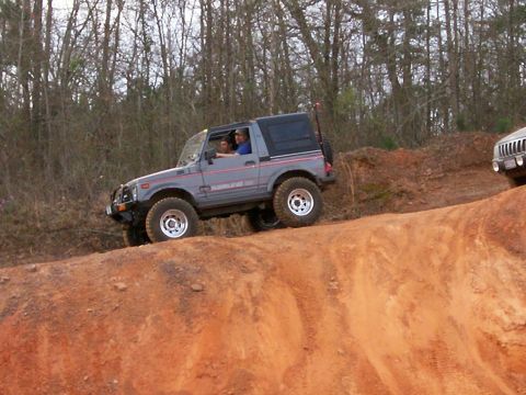 1993 Ford Bronco - Two people ride in a gray Suzuki Samurai as it navigates a dirt hill during an off-road event.