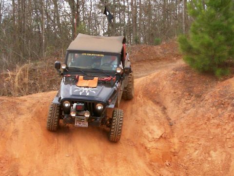 1993 Ford Bronco - A black Jeep Wrangler TJ navigates a steep, muddy incline on a wooded trail.