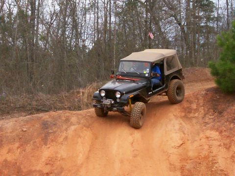 1993 Ford Bronco - A black Jeep CJ-7 navigates an off-road dirt path surrounded by trees.