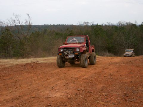 1993 Ford Bronco - A red Suzuki Samurai navigates a dirt trail with another vehicle visible in the distance.