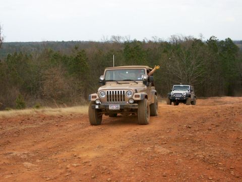 1993 Ford Bronco - Two Jeeps navigate a dusty trail through a wooded area.