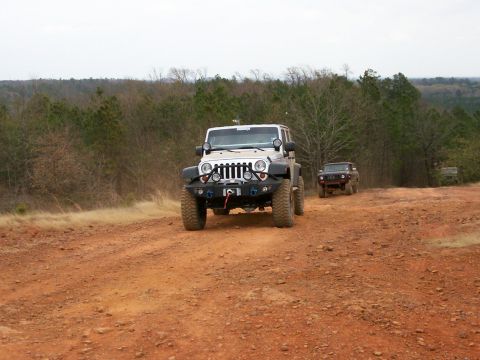 1993 Ford Bronco - Two off-road vehicles navigate a dusty trail through a wooded area.