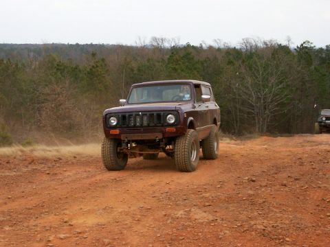 1993 Ford Bronco - An off-road vehicle drives on a dusty trail with trees in the background.