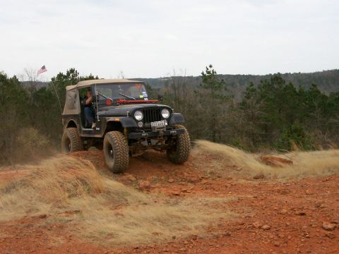 1993 Ford Bronco - A black Jeep CJ-7 navigates a dusty, off-road trail with a tan soft top and American flag.