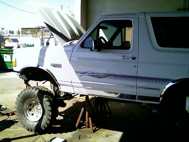 White 1996 Ford Bronco with hood open, lifted on jack stands, showing off its large tires
