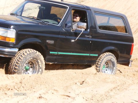 1993 Ford Bronco - A black Ford Bronco is stuck in the sand, with its tires partially buried.