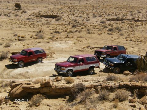 1993 Ford Bronco - Four Ford Bronco SUVs are parked in a desert landscape. The red and white Bronco in the foreground appears to be a 1993 model.