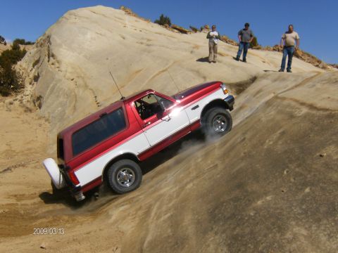 1993 Ford Bronco - A two-tone Ford Bronco navigates a steep, sandy off-road trail with spectators observing the climb.