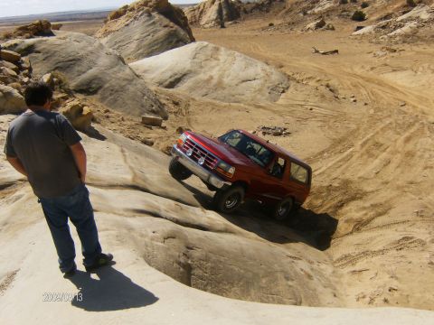 1993 Ford Bronco - A red SUV navigates a challenging off-road course with rocky terrain.
