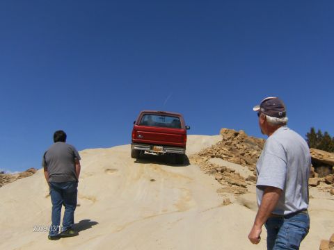 1993 Ford Bronco - A red 1993 Ford Bronco navigates a sandy incline under a clear blue sky.
